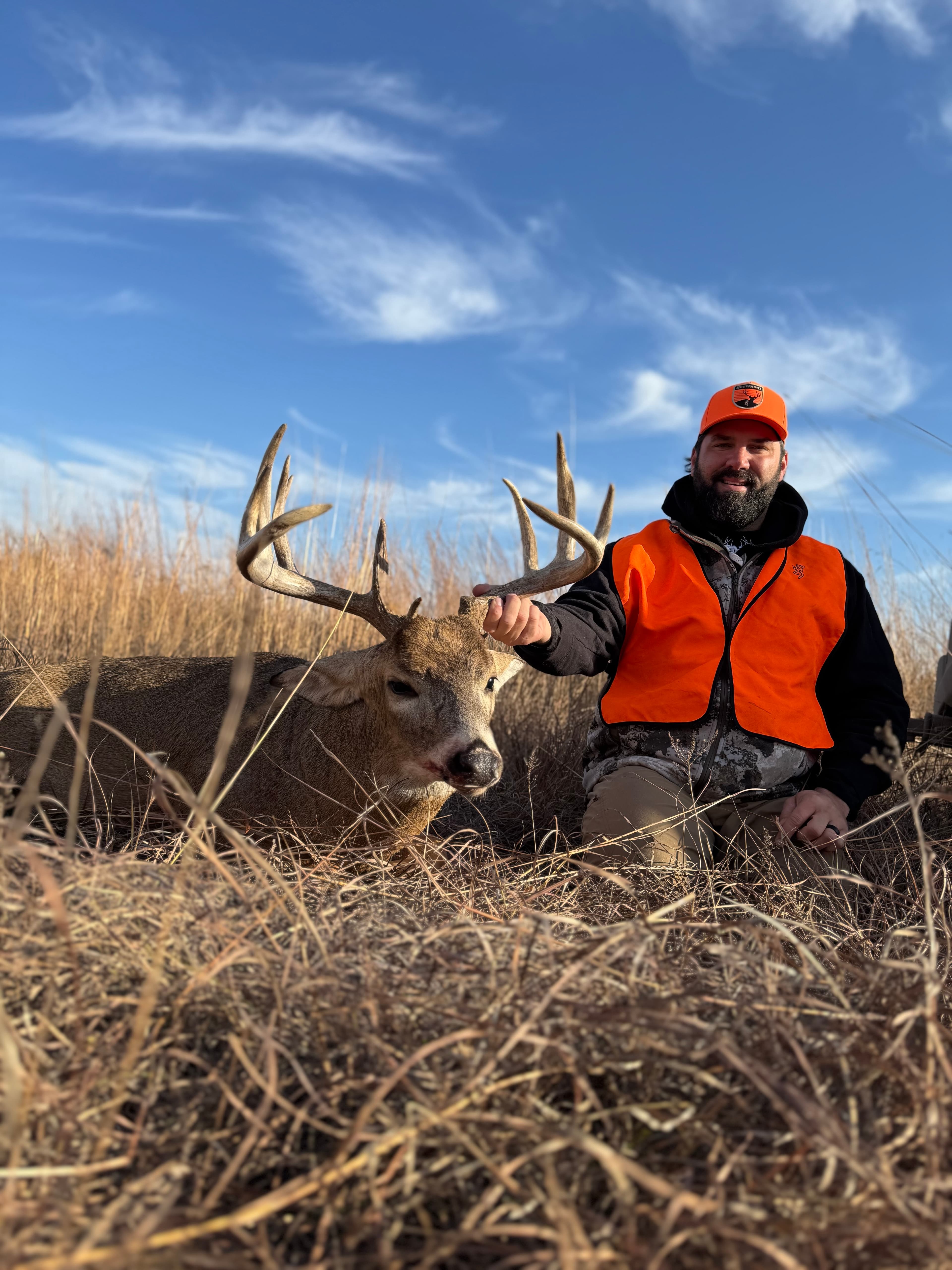 Hunter in blaze orange with a whitetail buck in Nebraska grasslands