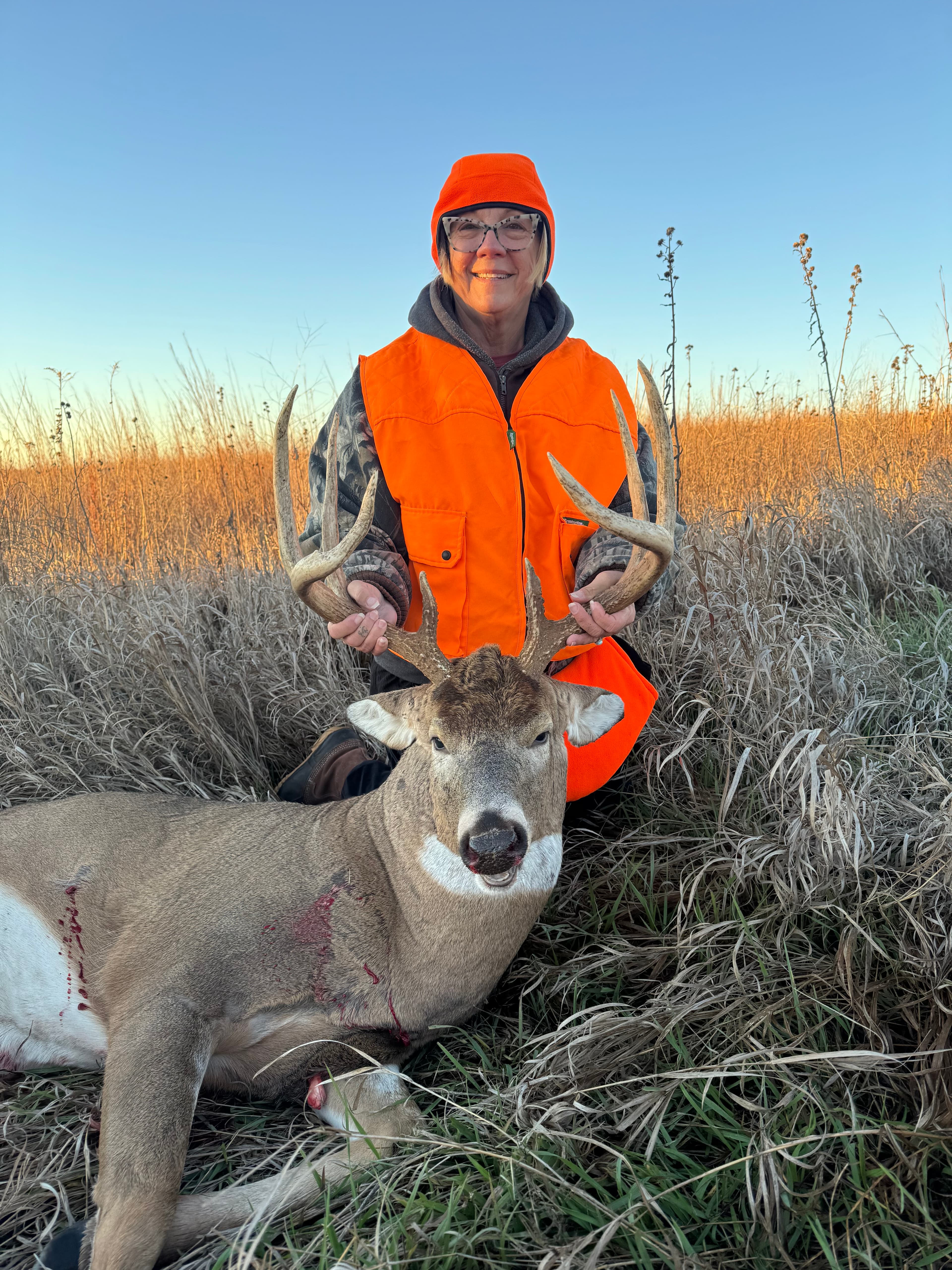 Hunter in blaze orange with a whitetail buck at sunset in Nebraska